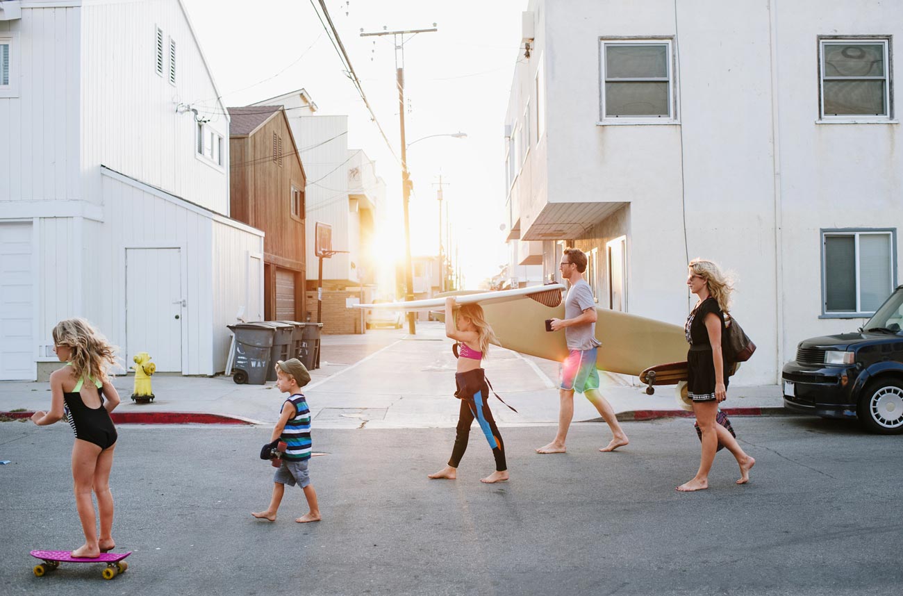 young family of five walking and skateboarding to beach through street
