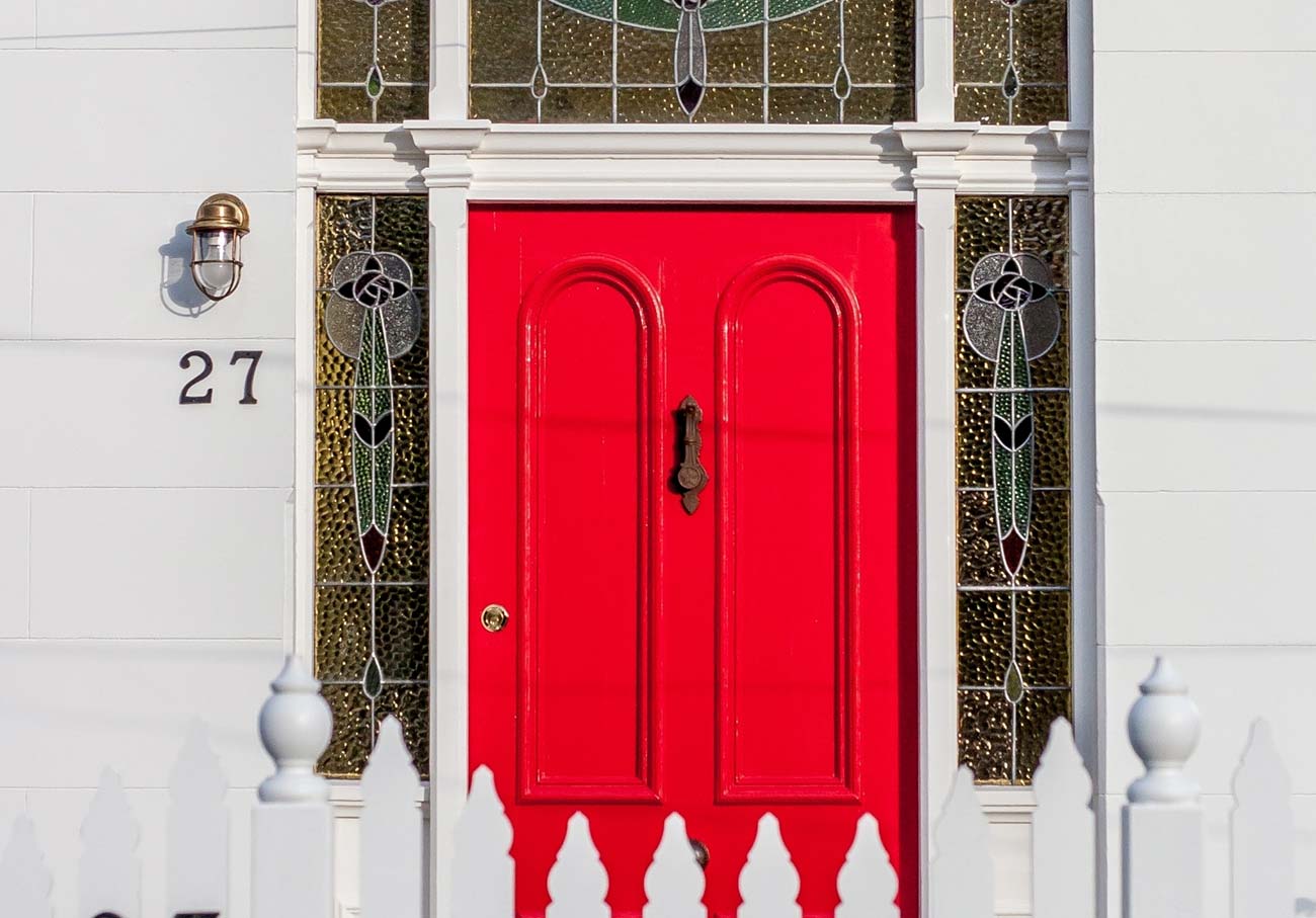 Red front door with white picket fence in urban streetscape