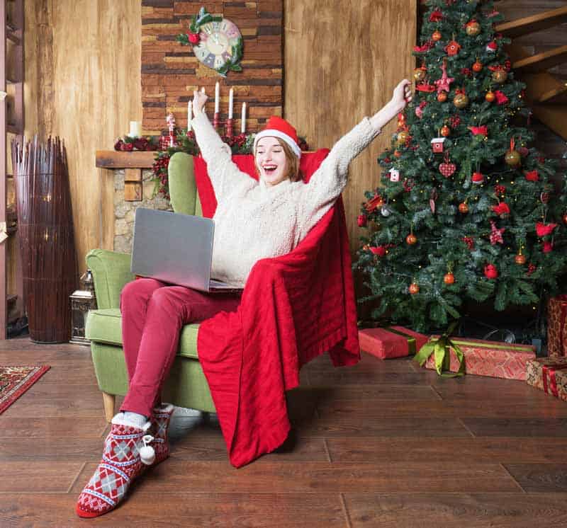 Young happy woman in red Christmas hat sitting with laptop