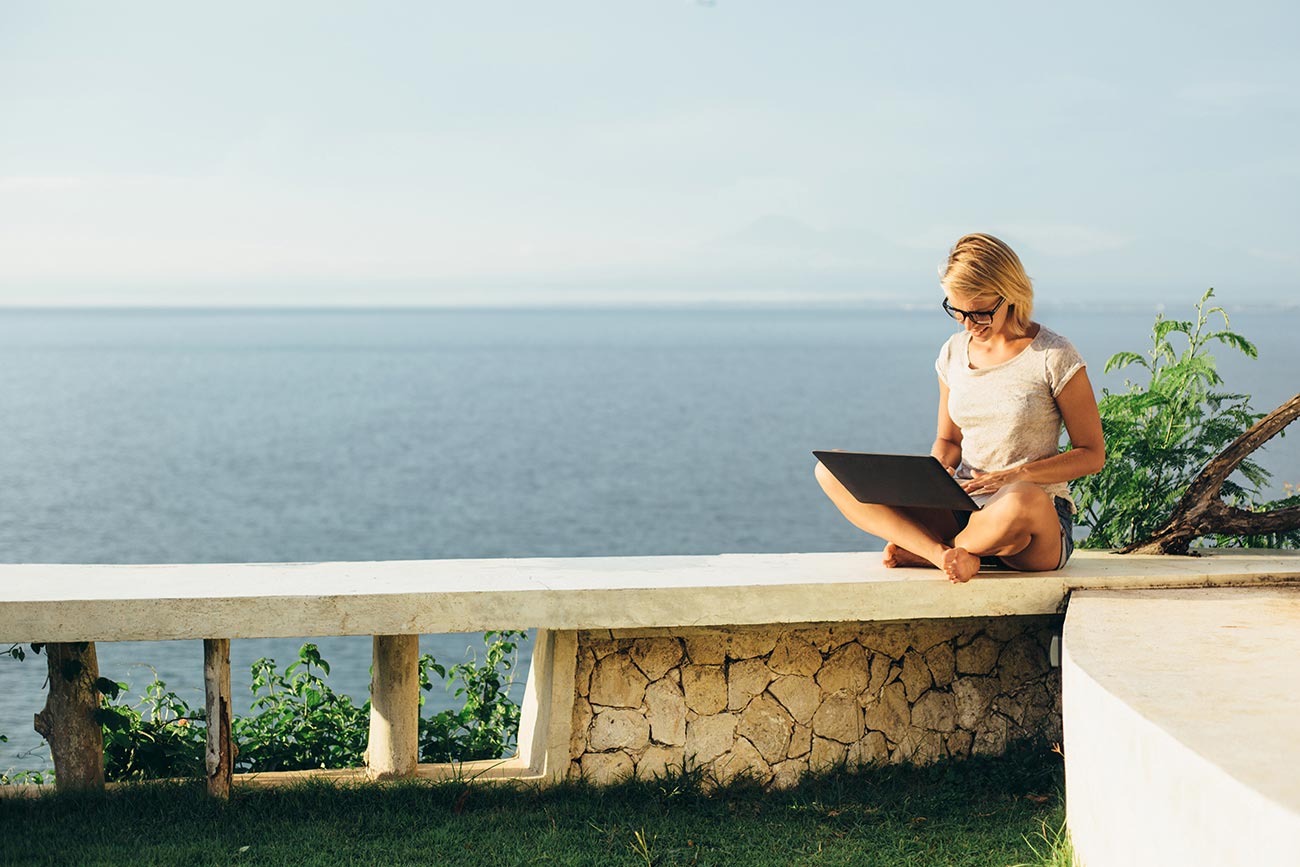 Blond girl working with a laptop on the tropical beach.