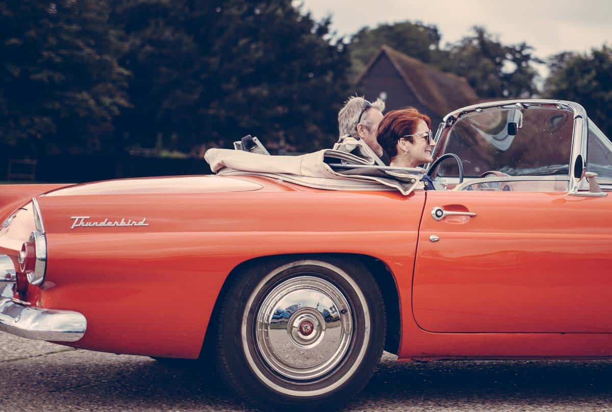 elderly couple riding in a red convertible