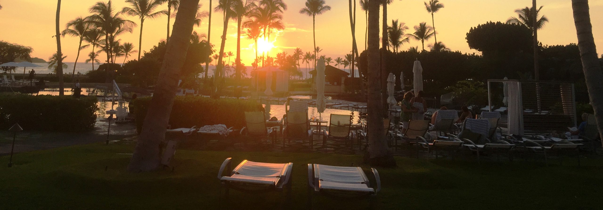 Sunset view by the pool with palm trees and sun loungers