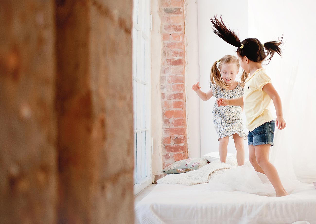 Two little girls are jumping on the bed