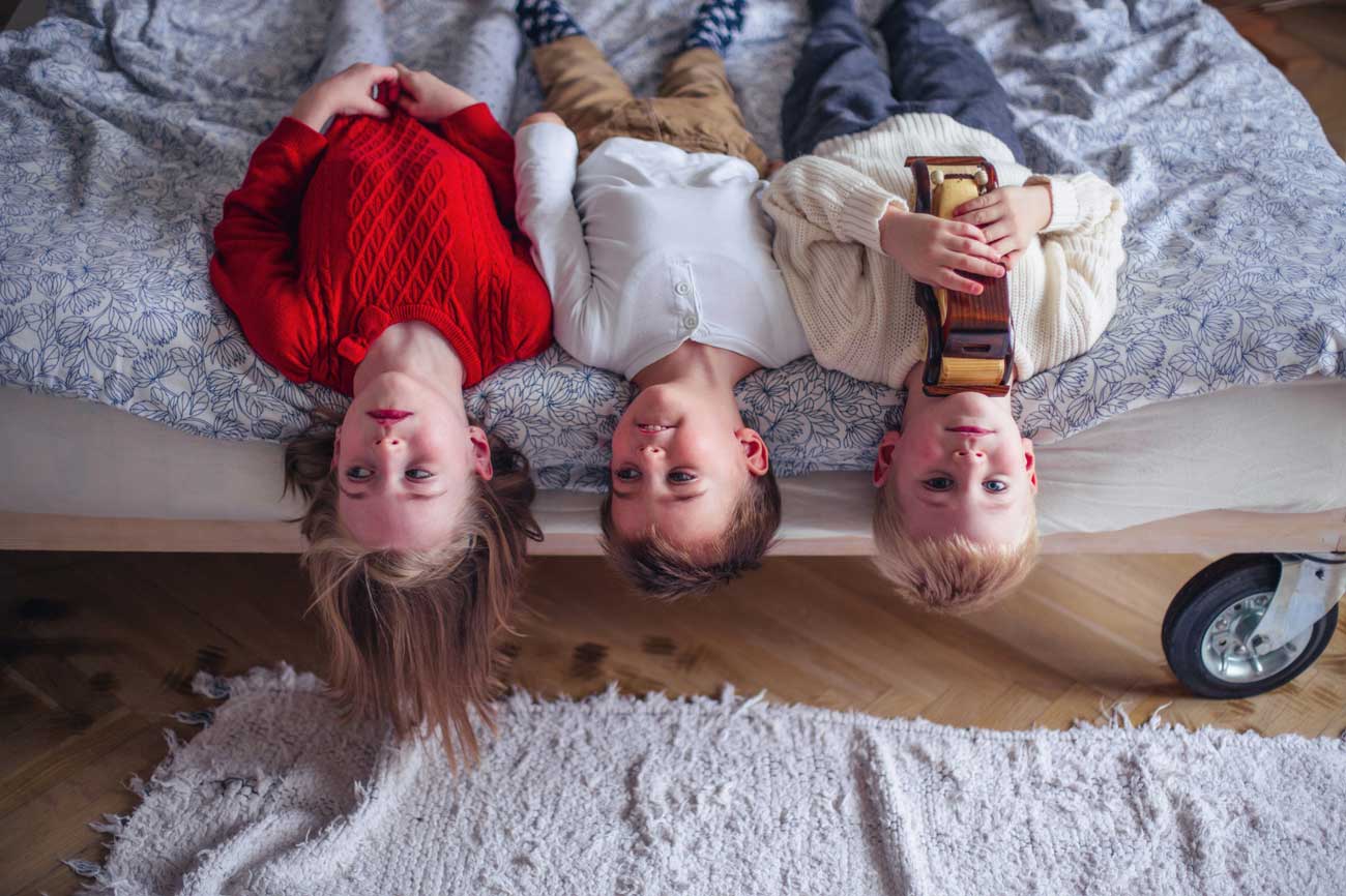 children laying upside down on the side of the bed