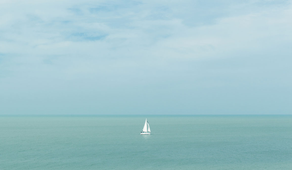 A sailboat on a clear and calm blue sea.